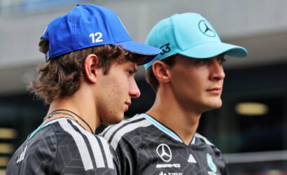 Two young men in Mercedes racing team jerseys stand side by side, wearing blue caps (one with 12, the other with 63) and sponsor logos on their shirts.
