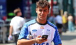Young man in a blue-and-white racing jersey outdoors, looking at his smartphone while holding a water bottle.