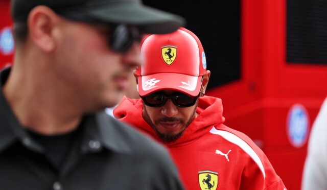 Man in a red Ferrari cap and hoodie with the crest, wearing sunglasses and looking downward.