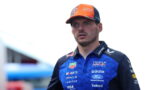 Portrait of a Formula 1 driver wearing a blue Oracle Red Bull Racing polo and an orange cap, looking surprised.