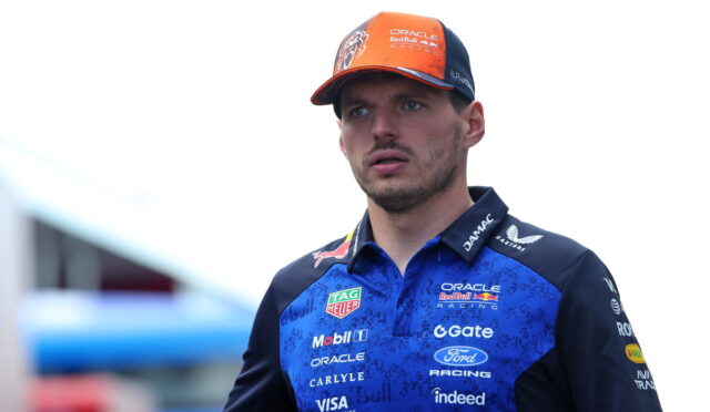 Portrait of a Formula 1 driver wearing a blue Oracle Red Bull Racing polo and an orange cap, looking surprised.