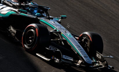 Mercedes-AMG Petronas Formula 1 car speeds around a corner on a race track, teal-silver livery and sponsor decals visible on the body.