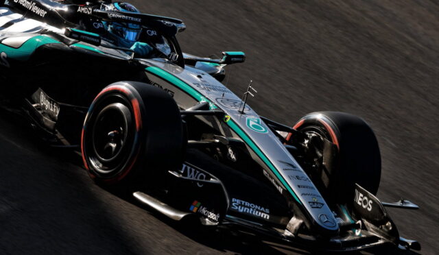 Mercedes-AMG Petronas Formula 1 car speeds around a corner on a race track, teal-silver livery and sponsor decals visible on the body.