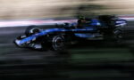 Blurred blue Formula 1 car speeding along track, motion blur conveying high speed and race action.
