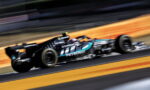 Mercedes-AMG Petronas Formula 1 car speeding on track with motion blur backdrop, sponsor logos visible like Petronas and Microsoft
