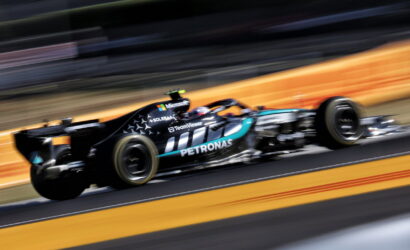 Mercedes-AMG Petronas Formula 1 car speeding on track with motion blur backdrop, sponsor logos visible like Petronas and Microsoft