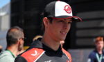 Young man in a black and red racing jersey and a white‑black cap smiling outdoors.