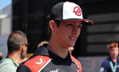 Young man in a black and red racing jersey and a white‑black cap smiling outdoors.