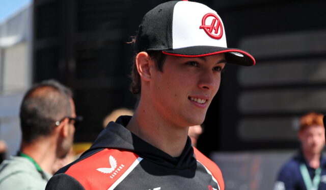Young man in a black and red racing jersey and a white‑black cap smiling outdoors.