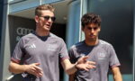 Two men in gray Revolut shirts stand outside a modern glass building; one wearing sunglasses speaks and gestures while the other listens.