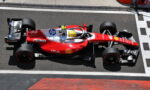 Red Ferrari Formula 1 car (#44) on a pit lane/track surface with a yellow-helmeted driver inside the cockpit, sponsor logos visible along the body.