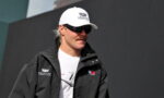 Man wearing a white Cadillac Formula 1 cap, black jacket, and sunglasses outdoors.