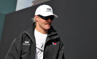 Man wearing a white Cadillac Formula 1 cap, black jacket, and sunglasses outdoors.