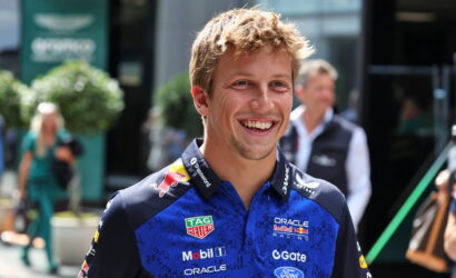 Smiling man in a Blue Red Bull Racing polo shirt with sponsor logos, standing outdoors at a race event (portrait).