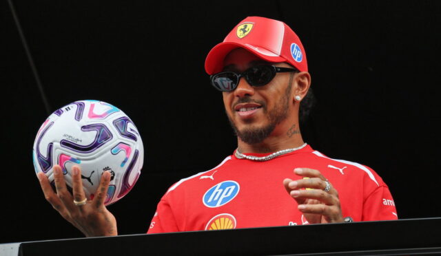 Athlete in a red cap and shirt on a podium, holding a patterned soccer ball.