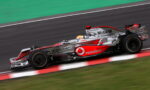 Formula 1 car in motion on the track, silver and red Vodafone livery, driver in a white helmet visible in the cockpit.