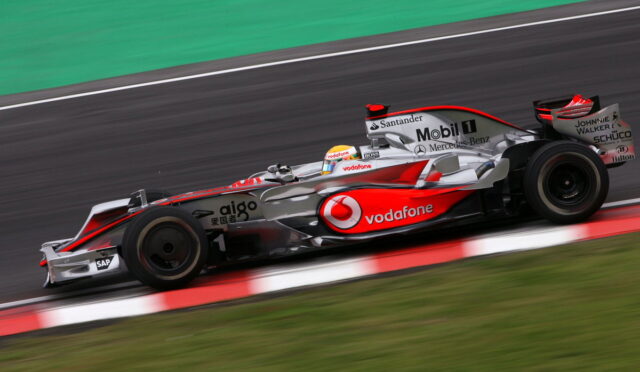 Formula 1 car in motion on the track, silver and red Vodafone livery, driver in a white helmet visible in the cockpit.