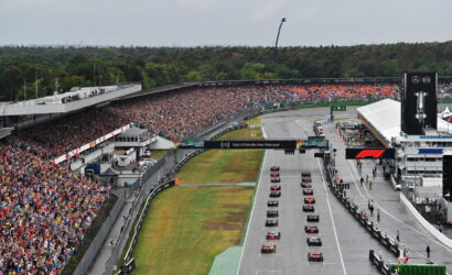 Wide shot of a Formula 1 race start: cars lined up on the starting grid as a packed grandstand watches.